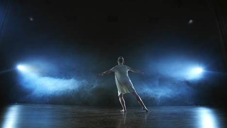 Modern-ballet-dancing-woman-barefoot-doing-spins-and-pirouettes-and-dance-steps-standing-on-stage-in-smoke-in-slow-motion.-Performance-on-stage.